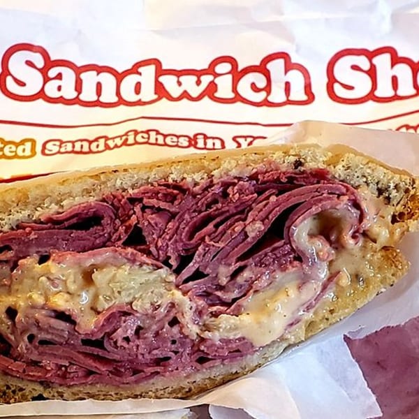 A close-up of a Pop's Sandwich Shop pastrami sandwich with melted cheese and sauerkraut.