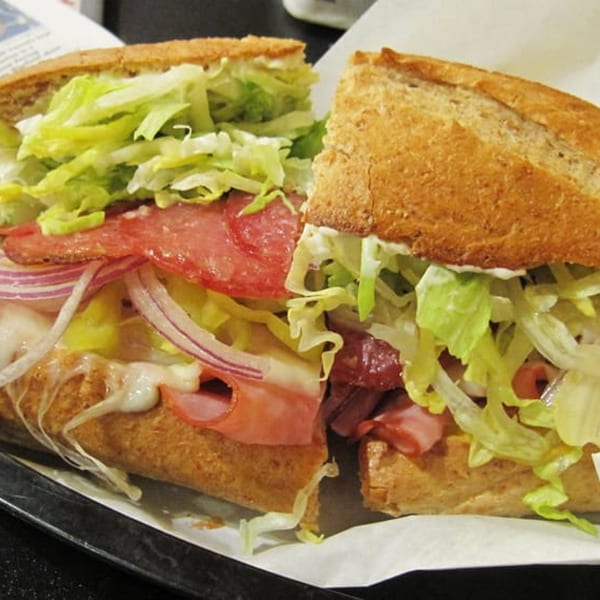 A Pop's Sandwich Shop sub sandwich, cut in half, with salami, ham, cheese, onions, and lettuce.